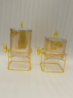 Two amber fluted glass beverage dispensers on gold metal stands resting on a modern kitchen counter
