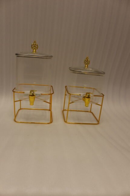 Two ribbed glass beverage dispensers with gold spigots and metal stands on a kitchen counter