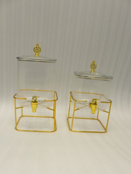 Two ribbed glass beverage dispensers with gold spigots and metal stands on a kitchen counter
