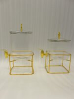 Two ribbed glass beverage dispensers with gold spigots and metal stands on a kitchen counter