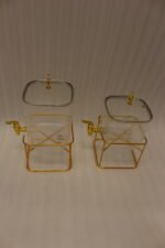 Two ribbed glass beverage dispensers with gold spigots and metal stands on a kitchen counter
