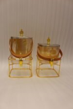 Amber shaded ribbed glass beverage dispenser with gold spigot, leather handle, and gold metal stand on a marble countertop