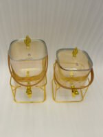 Two ribbed glass beverage dispensers with gold spigots, gold metal stands, decorative lids, and brown leather carrying straps on a marble kitchen counter.