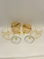 Two ribbed glass beverage dispensers with gold spigots, gold metal stands, decorative lids, and brown leather carrying straps on a marble kitchen counter.