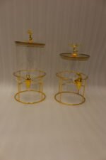 Two luxury clear glass beverage dispensers with gold deer lid handles and matching metallic stands on a marble countertop