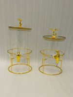 Two luxury clear glass beverage dispensers with gold deer lid handles and matching metallic stands on a marble countertop