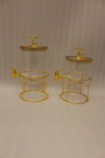 Two luxury clear glass beverage dispensers with gold deer lid handles and matching metallic stands on a marble countertop