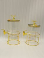 Two luxury clear glass beverage dispensers with gold deer lid handles and matching metallic stands on a marble countertop