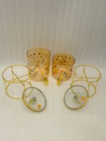 Two elegant clear glass drink dispensers with fruit prints, gold spigots, and gold deer lid handles resting on matching metal wire stands.