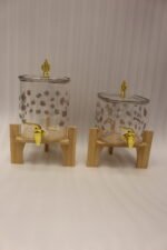 Clear floral patterned glass beverage dispenser with a gold spigot set on a modern wooden stand