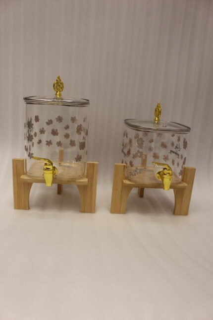 Clear floral patterned glass beverage dispenser with a gold spigot set on a modern wooden stand