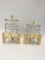 Clear floral patterned glass beverage dispenser with a gold spigot set on a modern wooden stand
