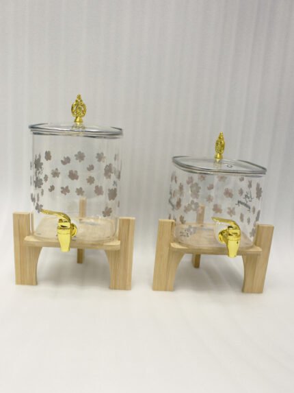 Clear floral patterned glass beverage dispenser with a gold spigot set on a modern wooden stand