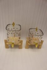 Clear floral patterned glass beverage dispenser with a gold spigot set on a modern wooden stand