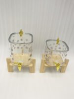 Clear floral patterned glass beverage dispenser with a gold spigot set on a modern wooden stand