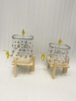 Clear floral patterned glass beverage dispenser with a gold spigot set on a modern wooden stand