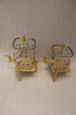 Clear floral patterned glass beverage dispenser with a gold spigot set on a modern wooden stand