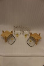Clear floral patterned glass beverage dispenser with a gold spigot set on a modern wooden stand