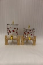 Two strawberry pattern glass drink dispensers with gold spigots set on wooden stands in a bright kitchen context.