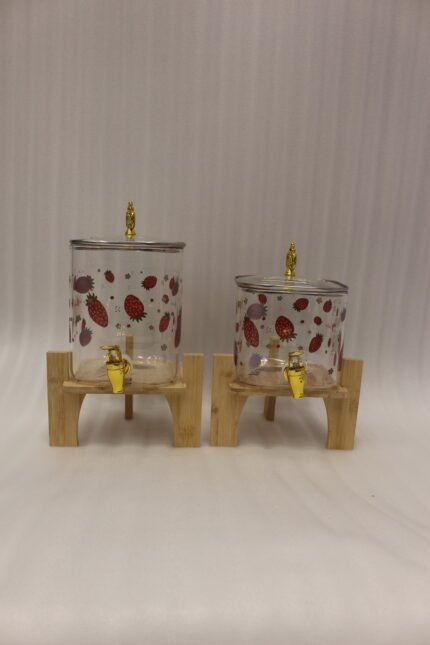 Two strawberry pattern glass drink dispensers with gold spigots set on wooden stands in a bright kitchen context.