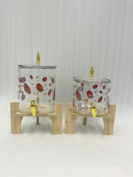 Two strawberry pattern glass drink dispensers with gold spigots set on wooden stands in a bright kitchen context.