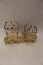 Two strawberry pattern glass drink dispensers with gold spigots set on wooden stands in a bright kitchen context.