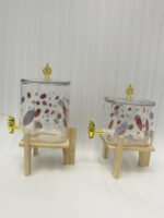 Two strawberry pattern glass drink dispensers with gold spigots set on wooden stands in a bright kitchen context.