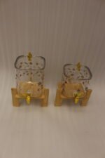 Two square glass beverage dispensers with fruit prints, gold spigots, and wooden stands on a kitchen counter