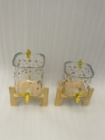 Two square glass beverage dispensers with fruit prints, gold spigots, and wooden stands on a kitchen counter