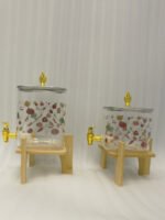 Two square glass beverage dispensers with fruit prints, gold spigots, and wooden stands on a kitchen counter