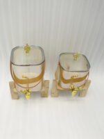 Two amber-shaded glass beverage dispensers with gold spigots, leather handles, and wooden stands on a kitchen counter.