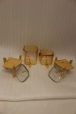 Two amber-shaded glass beverage dispensers with gold spigots, leather handles, and wooden stands on a kitchen counter.