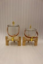 Ribbed glass beverage dispenser with leather carrying handle and gold spigot set on a wooden stand