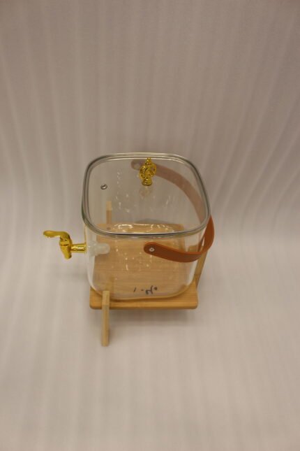 6.5-liter clear glass beverage dispenser with a gold spigot set on a raised wooden stand on a marble countertop