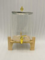 Clear 9.5L glass beverage dispenser with gold spigot on a wooden stand on a white marble countertop