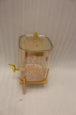 Amber glass drink dispenser with gold spigot resting on a natural wooden stand on a kitchen counter.
