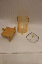 Amber glass drink dispenser with gold spigot resting on a natural wooden stand on a kitchen counter.