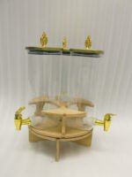 Triple glass beverage dispenser set featuring gold spigots, gold decorative lids, and a wooden rotating stand on a kitchen countertop.