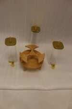 Triple glass beverage dispenser set featuring gold spigots, gold decorative lids, and a wooden rotating stand on a kitchen countertop.