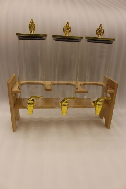 Triple clear acrylic beverage dispenser set on a wooden stand with gold spigots and decorative finial tops on a kitchen counter