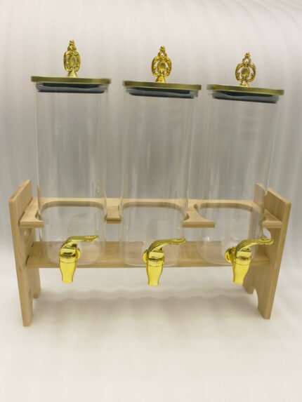 Triple clear acrylic beverage dispenser set on a wooden stand with gold spigots and decorative finial tops on a kitchen counter