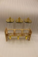 Triple clear acrylic beverage dispenser set on a wooden stand with gold spigots and decorative finial tops on a kitchen counter