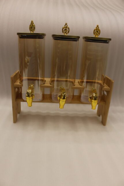 Triple 2.2L amber glass beverage dispenser set with ornate gold spigots and lids on a natural wooden stand on a marble countertop.