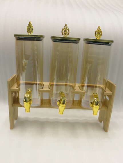 Triple 2.2L amber glass beverage dispenser set with ornate gold spigots and lids on a natural wooden stand on a marble countertop.