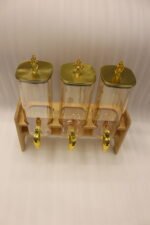 Triple 2.2L amber glass beverage dispenser set with ornate gold spigots and lids on a natural wooden stand on a marble countertop.