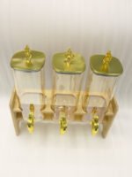 Triple 2.2L amber glass beverage dispenser set with ornate gold spigots and lids on a natural wooden stand on a marble countertop.