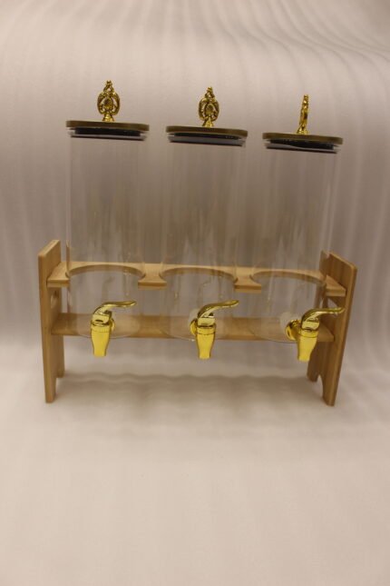 An elegant 3-tier beverage dispenser set featuring clear glass canisters with gold spigots and lids, resting on a natural bamboo stand on a white marble countertop.