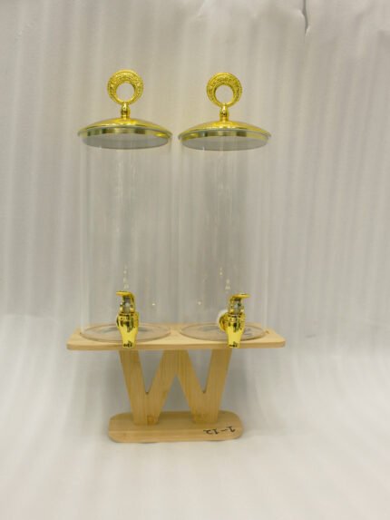 Two tall clear glass drink dispensers with gold spigots and circular gold finial lids resting on a wooden W-shaped stand.