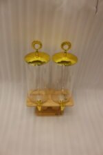 Two tall clear glass drink dispensers with gold spigots and circular gold finial lids resting on a wooden W-shaped stand.