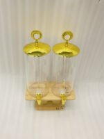 Two tall clear glass drink dispensers with gold spigots and circular gold finial lids resting on a wooden W-shaped stand.
